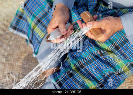 Der alte Mann strickt traditionelles Fischernetz, Hände im Rahmen Stockfoto