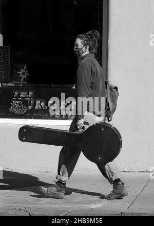 Eine junge Musikerin, die ihr Banjo trägt, geht zu einem Gig in Santa Fe, New Mexico. Stockfoto