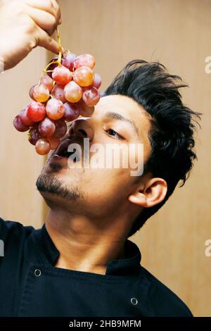 Junger indischer Koch posiert mit Trauben in Nahaufnahme Stockfoto