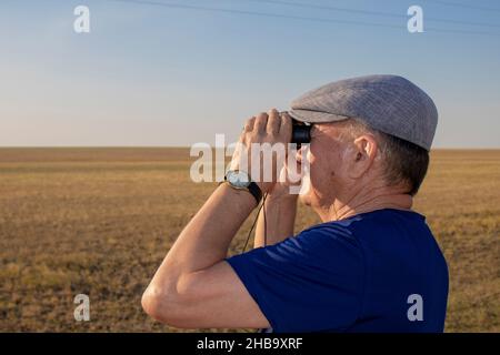 Älterer Mann schaut durch ein Fernglas in der Steppe Stockfoto