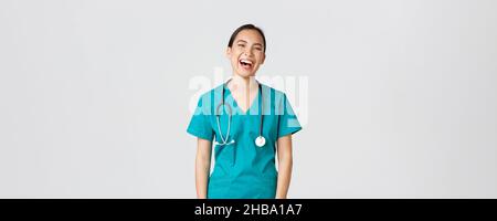 Covid-19, Mitarbeiter im Gesundheitswesen, Pandemiekonzept. Sorglos schöne weibliche asiatische Krankenschwester in Scrubs, Praktikant Spaß haben, lachen glücklich. Arzt beim Mittagessen Stockfoto