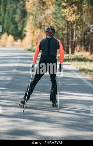 Training ein Athlet auf der Walze Skater. Biathlon Fahrt auf dem Roller Ski mit Skistöcke, im Helm. Herbst Training. Roller Sport. Stockfoto