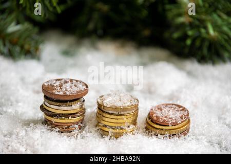 Eine goldene Pyramide von Münzen bedeckt mit Schnee vor einem Hintergrund von grünen Fichtenzweigen. Erfolgskonzept. Einsparungskonzept. Wohlstandskonzept im neuen Stockfoto