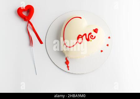 Ein Kuchen in Herzform. Mousse leichter Kuchen in Herzform mit der Aufschrift Liebe mit roten Herzen auf grauem Hintergrund. Valentinstag. Stockfoto