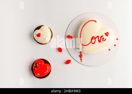 Valentinstag Hintergrund für Bäckerei, Süßwaren. Weißer Mousse-Kuchen und zwei kleine Kuchen in Herzform auf weißem Hintergrund. Stockfoto