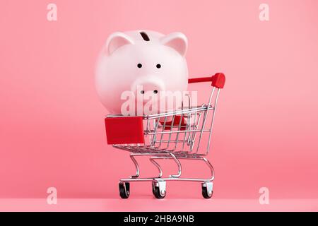 Pink Piggy Bank mit Einkaufswagen steht auf einem rosa Hintergrund. Online Business Shopping Konzept Stockfoto