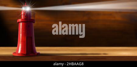 Alter roter Leuchtturm mit Lichtstrahlen auf einem leeren Holztisch, in einem dunklen Raum mit der braunen Holzwand im Hintergrund. Stockfoto