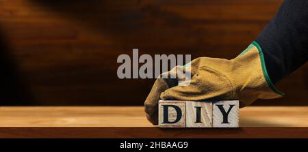 Arbeiter mit schützenden Arbeitshandschuhen, mit dem Text DIY (Do IT Yourself), aus Holzblöcken, über einer leeren Holzwerkbank mit Kopierfläche Stockfoto