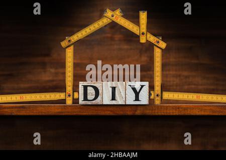 Nahaufnahme von DIY-Text aus Holzblöcken (Do IT Yourself) und einem klappbaren Lineal in Form eines Hauses auf einer hölzernen Werkbank mit Kopierraum. Stockfoto