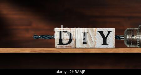 Nahaufnahme von DIY-Text (do it yourself), aus Holzblöcken und einer elektrischen Bohrmaschine mit schwarzer Spitze, über einem Holzregal oder einer Werkbank mit Kopierfläche. Stockfoto