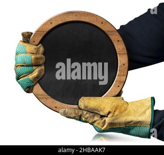 Hände mit schützenden Arbeitshandschuhen halten eine leere Tafel mit Holzrahmen und Nägeln in Form eines Kreises, isoliert auf weißem Hintergrund. Stockfoto