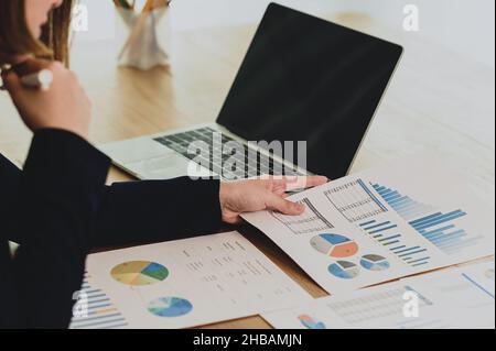 Geschäftsfrau, die Geschäftsdaten aus dem Diagramm analysiert, Geschäftsführerin, die den Datengraphen in der Hand betrachtet, Laptop und Dokumente auf einem Schreibtisch platziert, busi Stockfoto