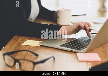 Geschäftsfrauen halten den Stift auf der Laptop-Tastatur, eine Frau hält den Stift und den Kaffeebecher auf dem Schreibtisch, Geschäftskonzept, Nahaufnahme Stockfoto