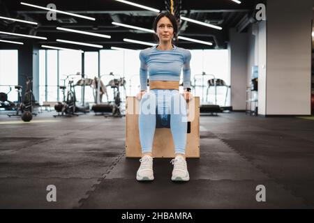 Eine athletische Frau in blauer Sportbekleidung macht Trizeps-Übungen auf einer hölzernen Crossfit-Sprungbox im Fitnessstudio Stockfoto