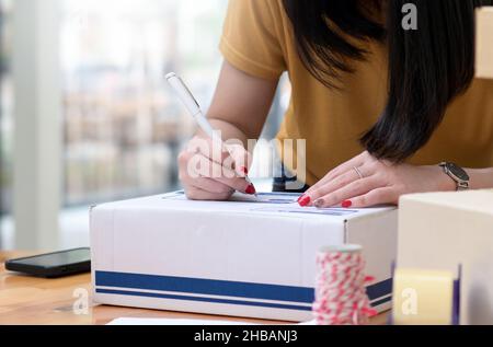 Die ausgeschnittene Aufnahme Einer jungen Frau schreibt eine Adresse auf die Box, um Pakete zu liefern, Pakete zu transportieren. Stockfoto