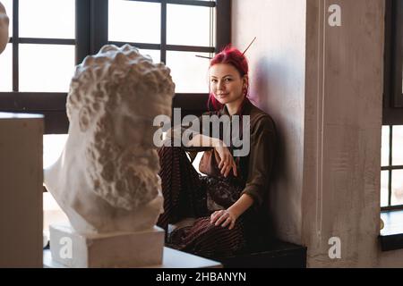 Junge Künstlerin, die auf einer Fensterbank in einem Kunststudio sitzt Stockfoto