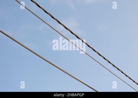 Ein Porträt von elektrischen Hochspannungskabeln vor blauem Himmel. Die Stromleitungen verlaufen diagonal über dem Bild. Stockfoto