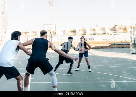 Frau und drei Männer spielen Basketball in einem städtischen Gericht Stockfoto