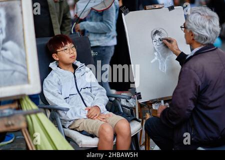 Paris, Frankreich - August 2019: asiatischer Junge, der von einem Maler von Montmartre am Place du Tertre, wenige Straßen von der Basilika von Montmartre, porträtiert wird Stockfoto