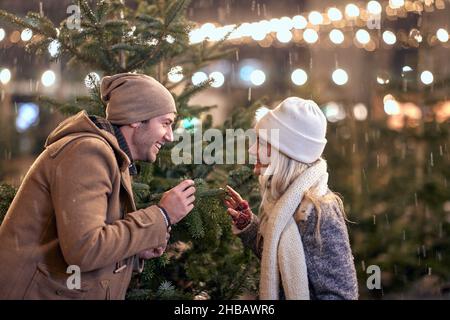 Ein junges Paar genießt Weihnachtsferien, während es in einer wunderschönen verschneiten Nacht durch die Stadt geht. Weihnachten, Neujahr, Urlaub, Liebe Stockfoto