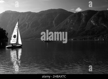 Segelboot und Touristenboot auf dem Bohinjer See im Sommer, Triglav Nationalpark, Slowenien. Schwarzweiß-Bild Stockfoto