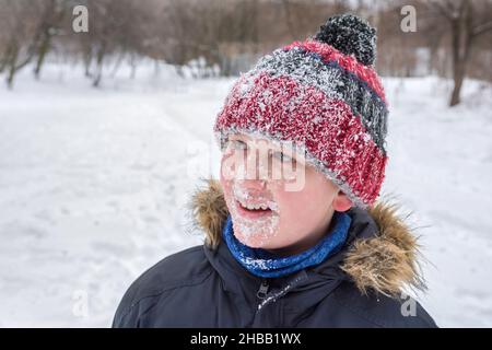 Porträt eines glücklichen Jungen im Winter auf einem Hintergrund von Schnee. Alles Gesicht im Schnee. Stockfoto