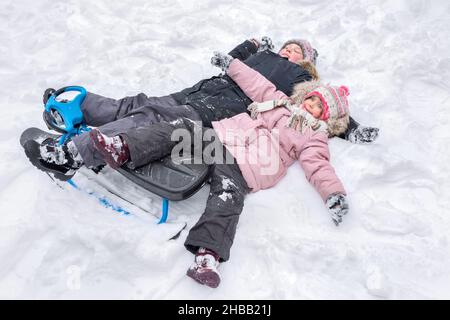 Ein glücklicher Junge und ein Mädchen liegen zusammen im Schnee und machen Schneeengel. Stockfoto