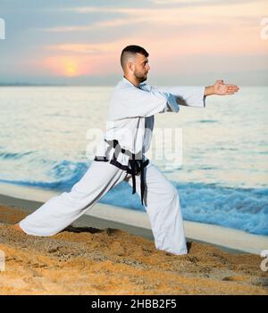 Mann in Uniform macht Taekwondo-Übungen an der Küste bei Sonnenuntergang Stockfoto