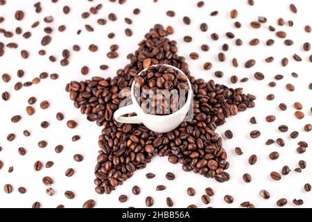 Tasse Kaffee und Stern aus gerösteten Kaffeebohnen auf weißem Hintergrund. Verstreute Kaffeebohnen. Stockfoto