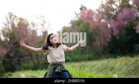 Das asiatische Mädchen lächelt verschmitzt und wendet sich während einer Naturtour der Kamera zu, sie spreizte beide Arme. Stockfoto