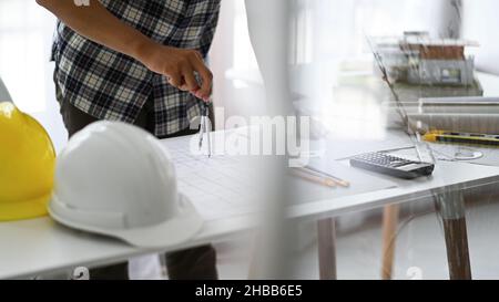 Designer verwenden Kompasse, um Entwürfe auf Häuserpläne, Hauspläne und Schutzhelme mit Zeichenwerkzeugen auf den Tisch zu zeichnen. Stockfoto