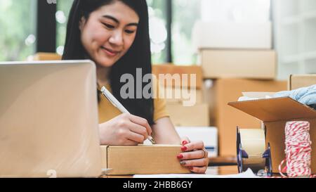 Frau schreibt eine Adresse auf einem Paketkasten für die Lieferung an einen Kunden, Verkaufen Produkte online, Transport von Paketen. Stockfoto