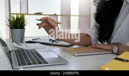 Frau hält einen Stift in der Hand, zeigt auf einen Laptop-Bildschirm, sie verwendet einen Laptop und Rechner eine Arbeitsanalyse, Rechner und Laptop und Notebook auf dem Stockfoto