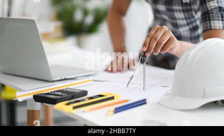 Designer nutzen den Kreisverkehr, um Hausentwürfe zu zeichnen, junger Architekt, der den Kreisverkehr nutzt, um auf den Bauplan zu schreiben, Laptop mit Zeichenwerkzeugen und eine SA Stockfoto