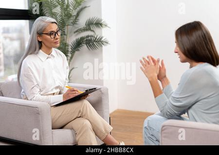 Gescheiterte junge Patientin, die während der Therapiesitzung mit einer asiatischen Seniorpsychotherapeutin über Probleme und Ängste sprach. Konzept der psychischen Gesundheit Stockfoto