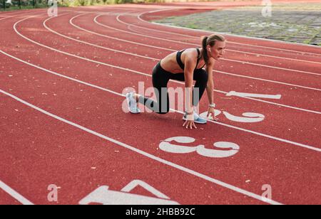 Junge Läuferin Frau in Sportbekleidung, die sich bereit für den Sprint bei niedrigem Start auf der Stadion-Strecke mit rot beschichtet Stockfoto