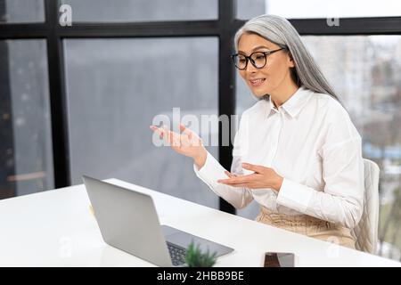 Eine ältere Geschäftsfrau, die einen Laptop für Online-Videobesprechung mit Kollegen verwendet. Der leitende Lehrer führt Kurse und Webinare durch. Eine ältere Dame, die an der Rezeption sitzt und bei der Online-Konferenz spricht Stockfoto