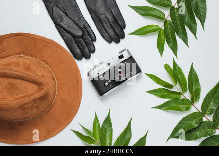 Reisen im Herbst. Damenzubehör, Retro-Kamera auf weißem Hintergrund mit grünen Blättern. Filzhut, Lederhandschuhe. Draufsicht Stockfoto