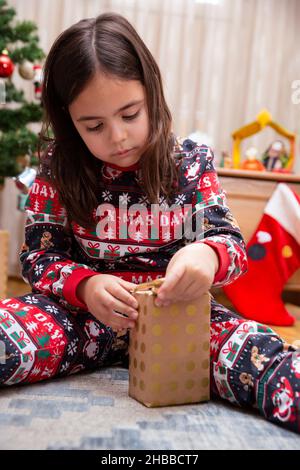 Porträt von 6 Jahre alten kaukasischen Mädchen unterhaltsam Eröffnung eines Weihnachtsgeschenk. Stockfoto