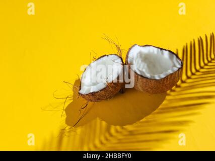 Minimalistisches tropisches Stillleben. Zwei Hälften gehackte Kokosnuss mit Schatten von Palmblättern auf gelbem Hintergrund. Kreatives Modekonzept. Stockfoto