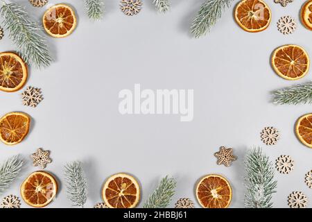 Rahmen mit winterlichen Tannenzweigen, getrockneten Orangenscheiben und Schneeflocken auf grauem Hintergrund mit Kopierraum Stockfoto