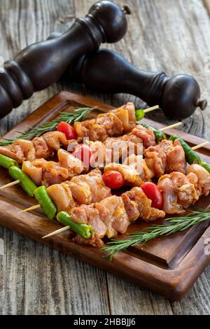 Hähnchenspieße auf einem hölzernen Hintergrund. Nahaufnahme von rohen Hähnchenspießen, mariniert in Tomatensauce. Vertikale Ansicht. Textformat Stockfoto