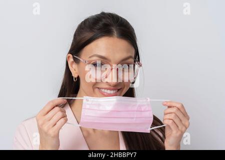 Salisbury, Wiltshire, Großbritannien. 2021. Frau mit Brille, die während des Covids eine rosafarbene medizinische Maske auf ihr Gesicht legt. Stockfoto