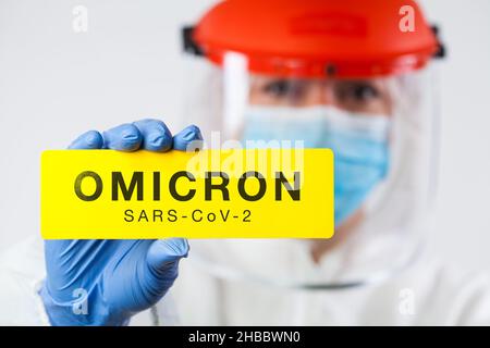 Genetische Mutation des Coronavirus verursacht neue COVID-19 Fälle, medizinisches Personal trägt PSA und Gesichtsschutz mit gelbem SARS-CoV-2 OMICRON-Schild Stockfoto