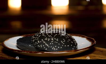 Nahaufnahme von schwarzem Brot mit Sesam, das auf einem Teller auf dem Holztisch liegt. Hausgemachtes Brot für die Hamburger-Zubereitung. Stockfoto