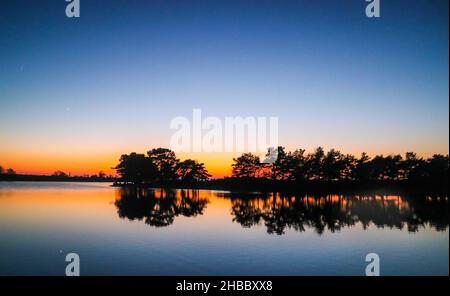 New Forest, Hampshire, UK 18 December 2021 Hatchet Pond herrlicher Sonnenuntergang., mit dem ersten Stern des Abends, der auf dem Wasser reflektiert Paul Quezada-Neiman/Alamy Live News Stockfoto