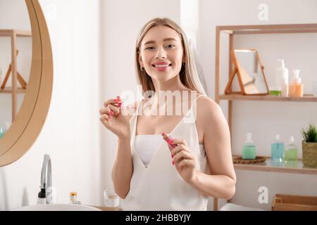Hübsche junge Frau mit Lippenstift im Badezimmer Stockfoto