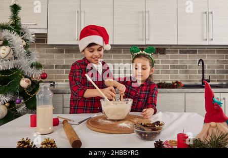 Gutaussehende kaukasische Kinder, schönes Kindermädchen und gutaussehender Schuljunge, liebevoller Bruder und Schwester, die zusammen den Weihnachtsteigteig zubereiten Stockfoto