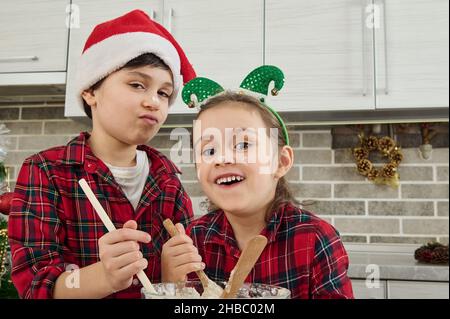 Fröhliche niedliche Kinder verwöhnen, haben Spaß zusammen in der Küche zu Hause, bereiten Teig für Weihnachtskuchen und Kekse. Die Kinder selbst sind in der Stockfoto