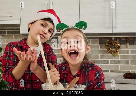 Fröhliche niedliche Kinder verwöhnen, haben Spaß zusammen in der Küche zu Hause, bereiten Teig für Weihnachtskuchen und Kekse. Die Kinder selbst sind in der Stockfoto